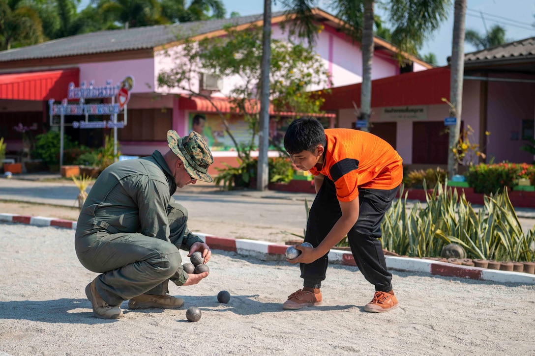 A Marine and a child collect balls off the ground.