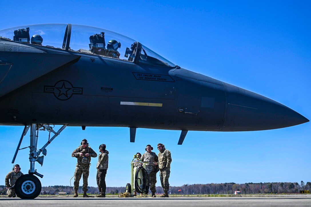 Airmen stand underneath a parked aircraft.