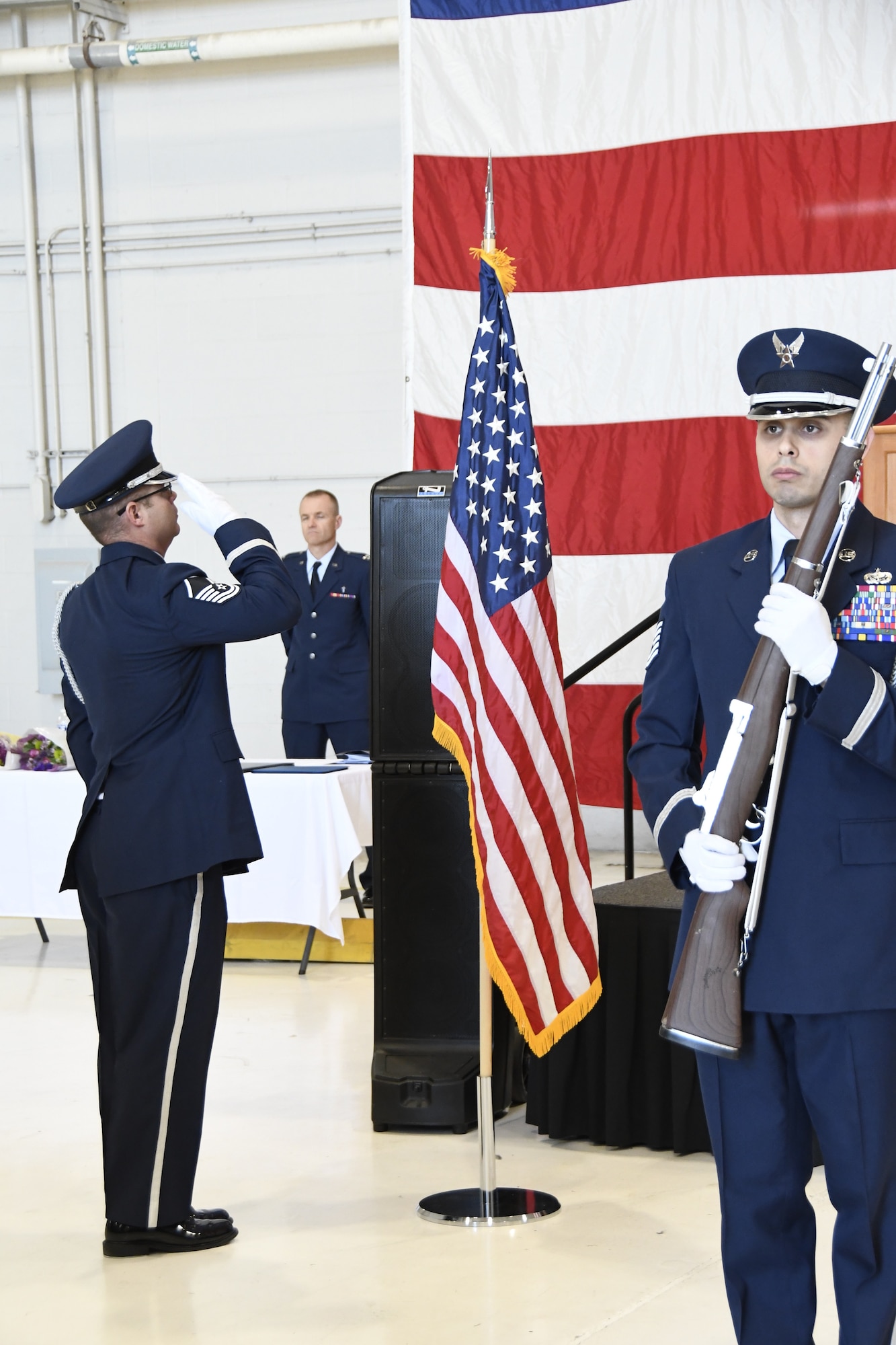 One Honor Guard member salutes a small flag while another stand at attention with honor guard riffle.