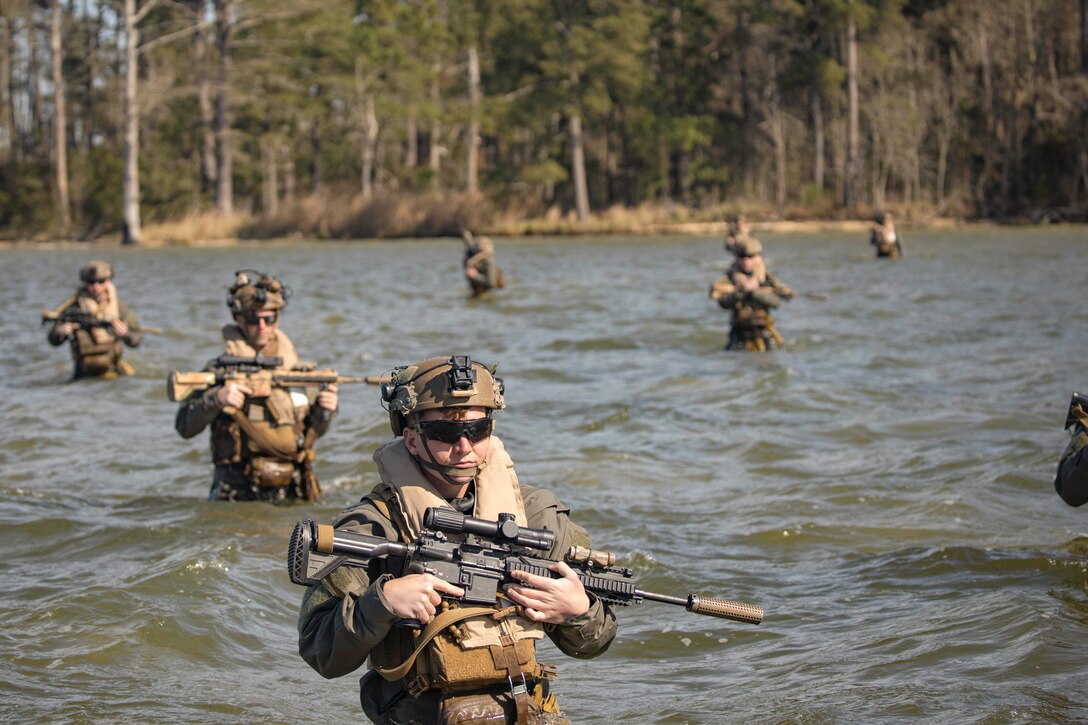 Marines hold weapons while standing in a body of water.