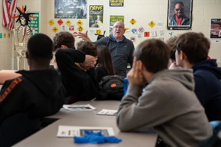 Man standing at the front of a classroom, giving a presentation.