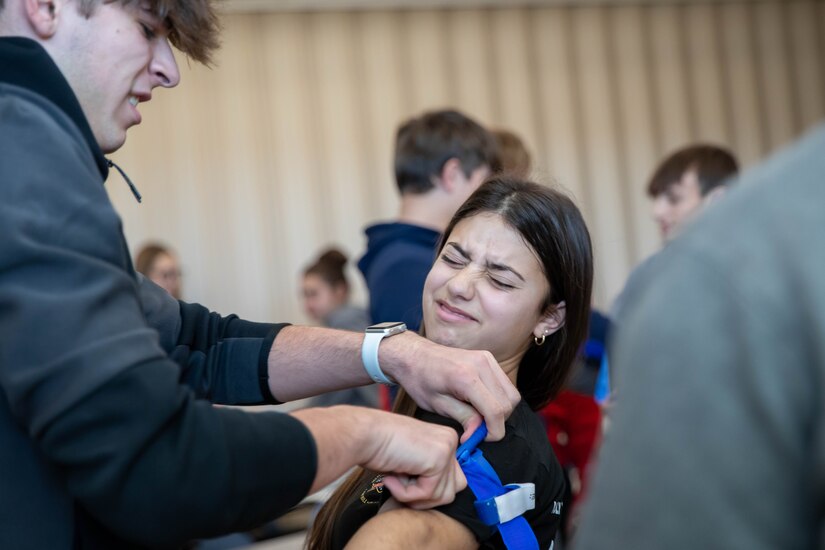 a female student's arm is wrapped in bandages by a male student.