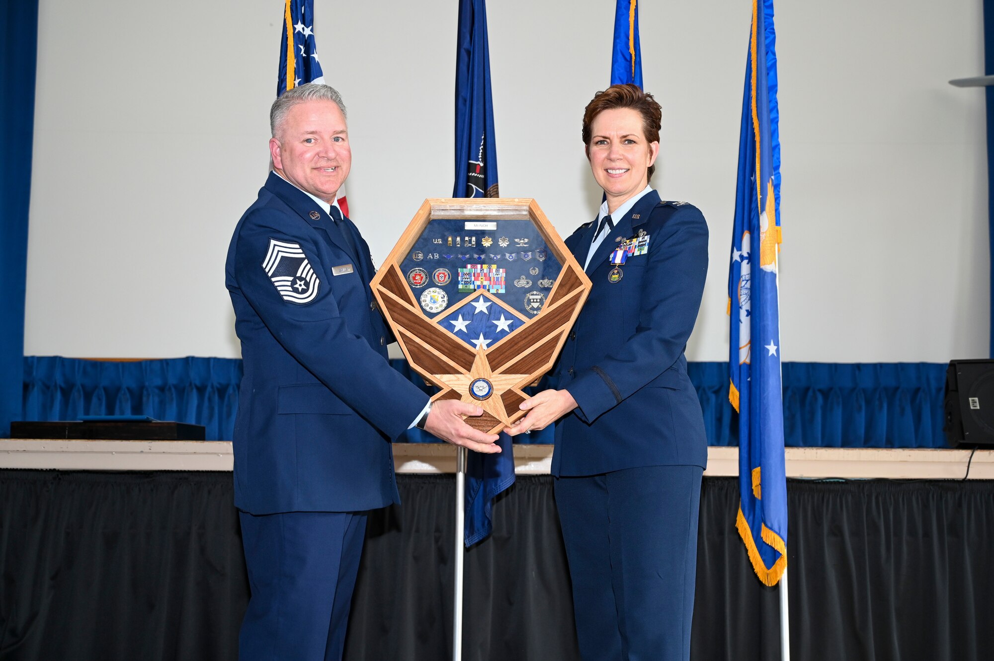 A man in Air Force Dress blues hands a woman in Air Force Dess blues, a shadow box.