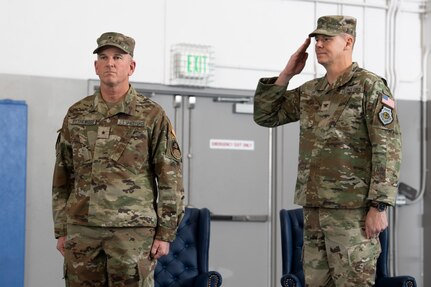 Man in uniform standing at attention next to man in uniform saluting