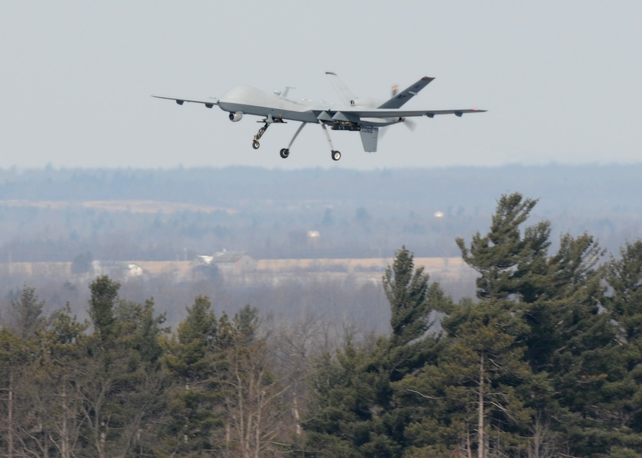 An unmanned aircraft is shown hovering above a tree line.