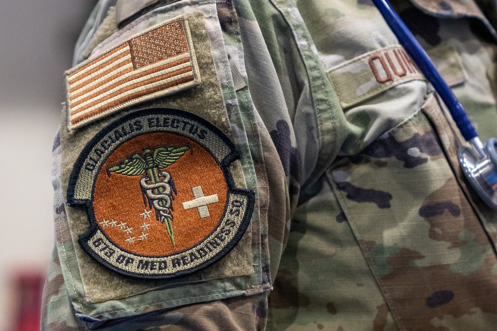 A circular patch depicting medical imagery and the Big Dipper sits below an American Flag patch on the side of a uniform