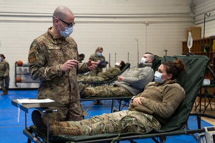U.S. Air Force Senior Airman Justin Kirk stands next to a patient laying in a cot.