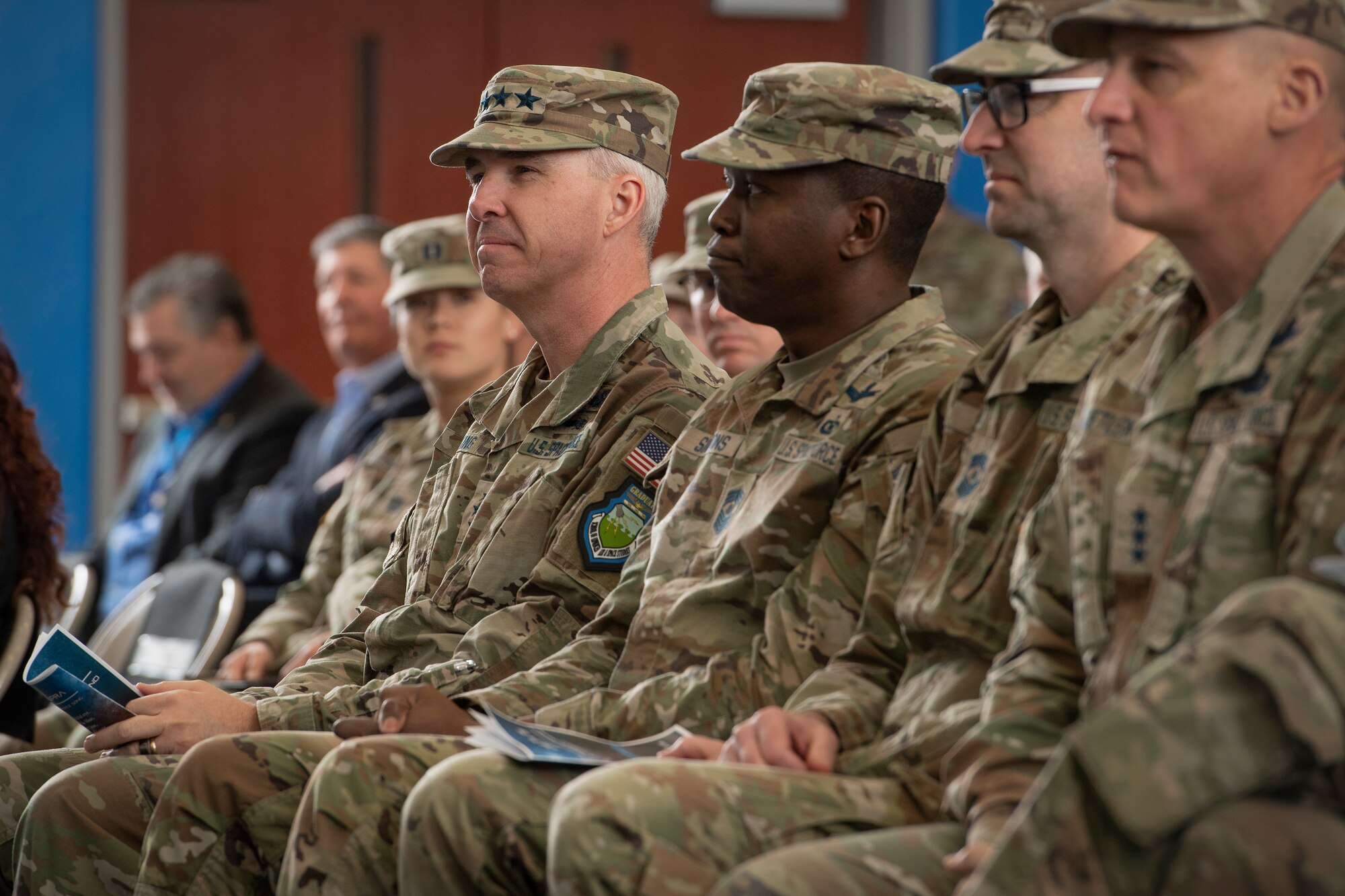 Four military men in uniform sitting and watching a ceremony