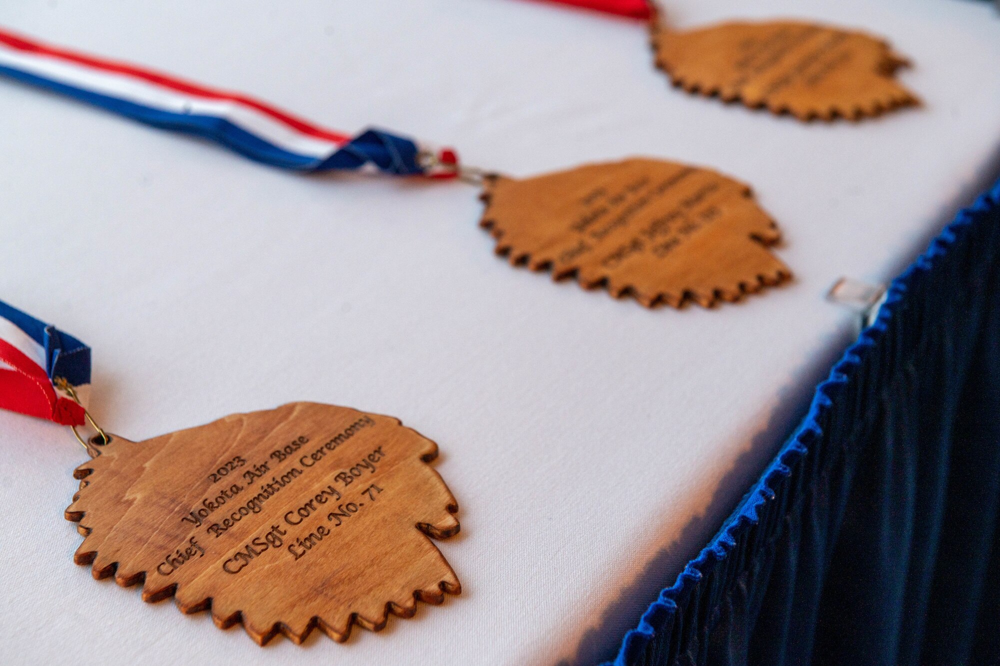 A leaf-shaped medallion attached to a red, white, and blue-ribbon rests on a table covered in a white cloth.