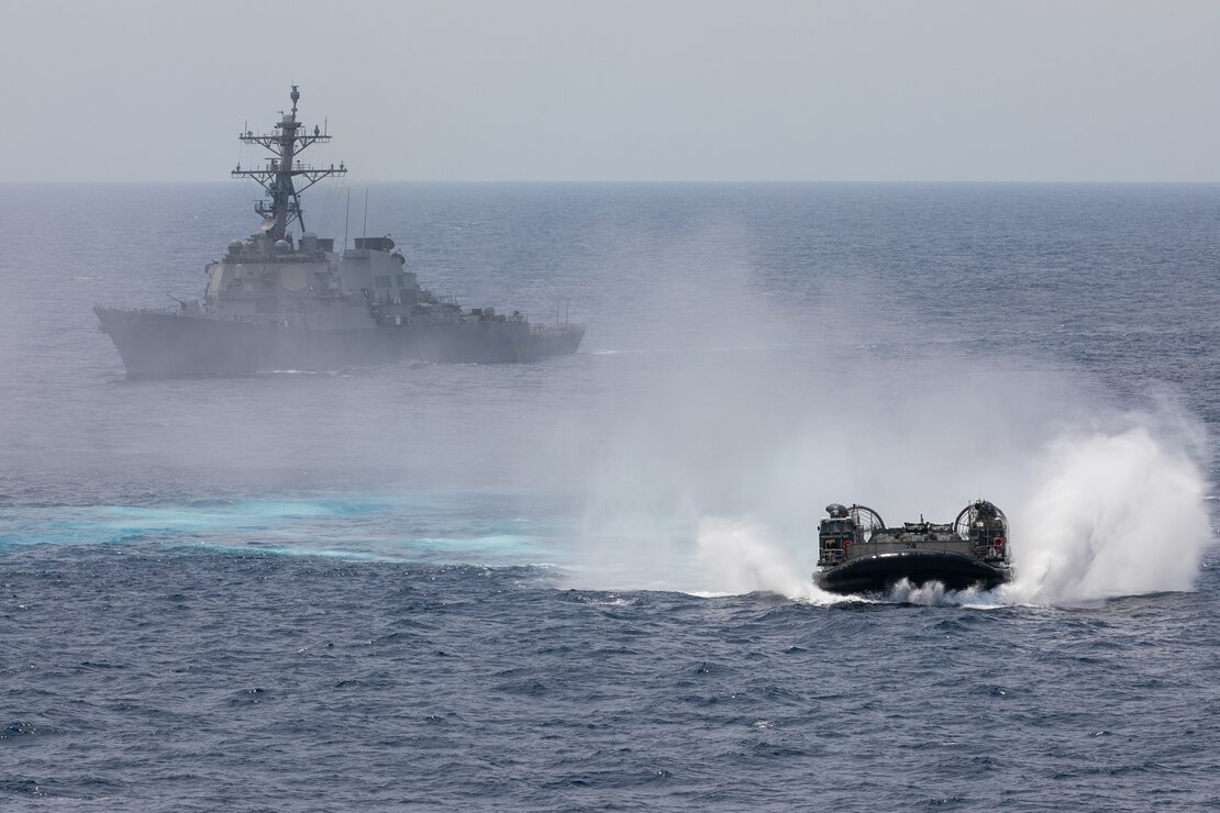A landing craft air cushion (LCAC) from Assault Craft Unit (ACU) 5 maneuvers in front of the Arleigh Burke-class guided-missile destroyer USS Decatur (DDG 73). Nimitz Carrier Strike Group (NIMCSG) and Makin Island Amphibious Ready Group (MKI ARG), with embarked 13th Marine Expeditionary Unit (MEU), are conducting combined expeditionary strike force (ESF) operations, demonstrating unique high-end war fighting capability, maritime superiority, power projection and readiness.