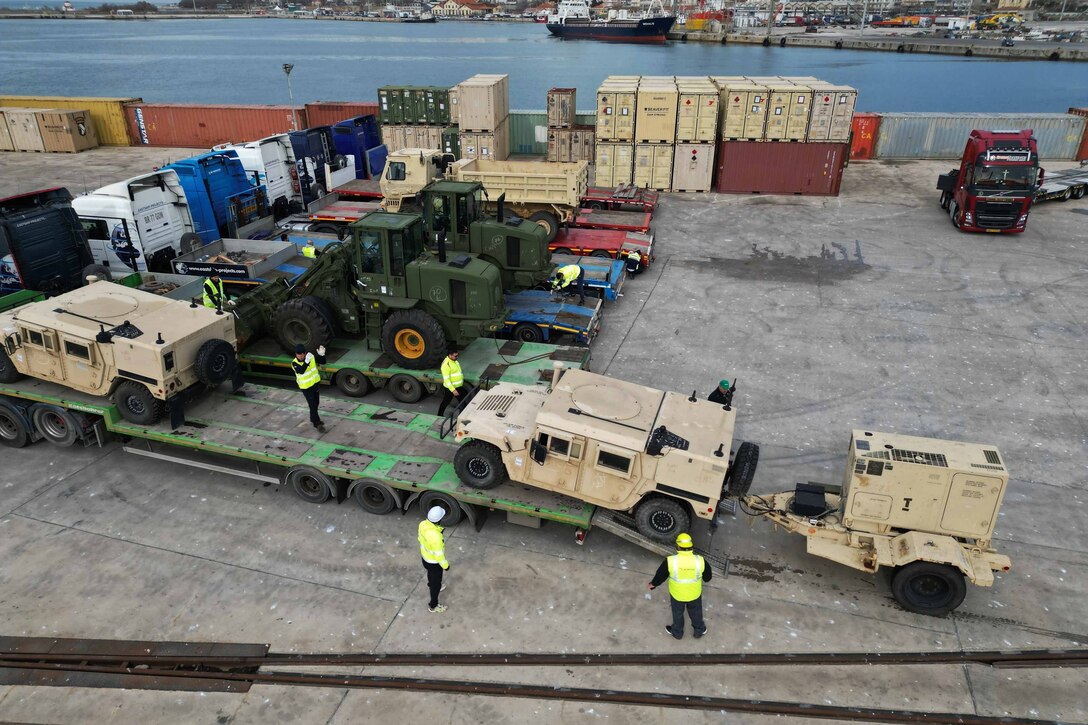 Soldiers move vehicles and equipment onto a ramp.