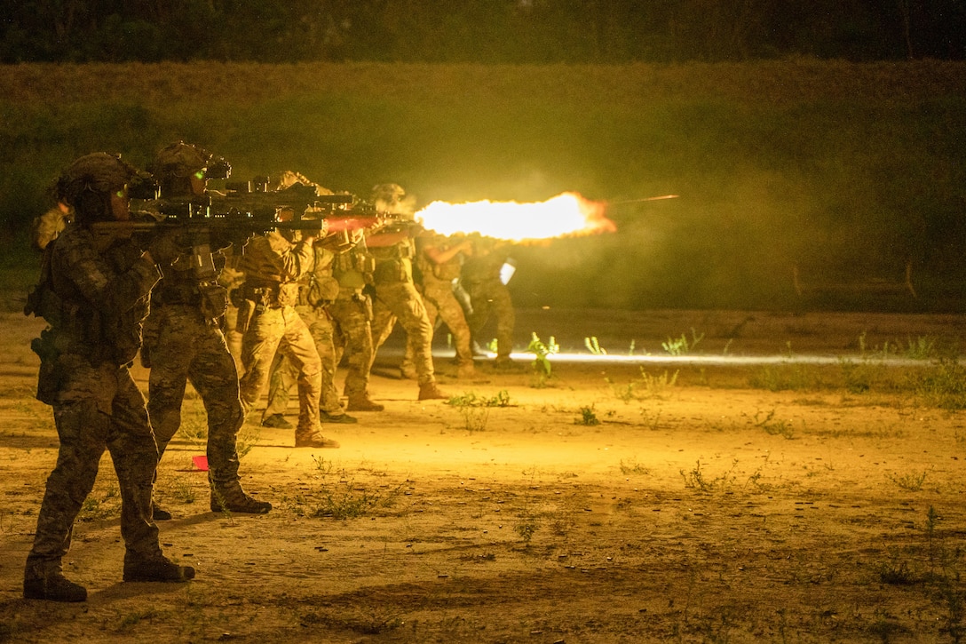 A line of soldiers fire their weapons at night.