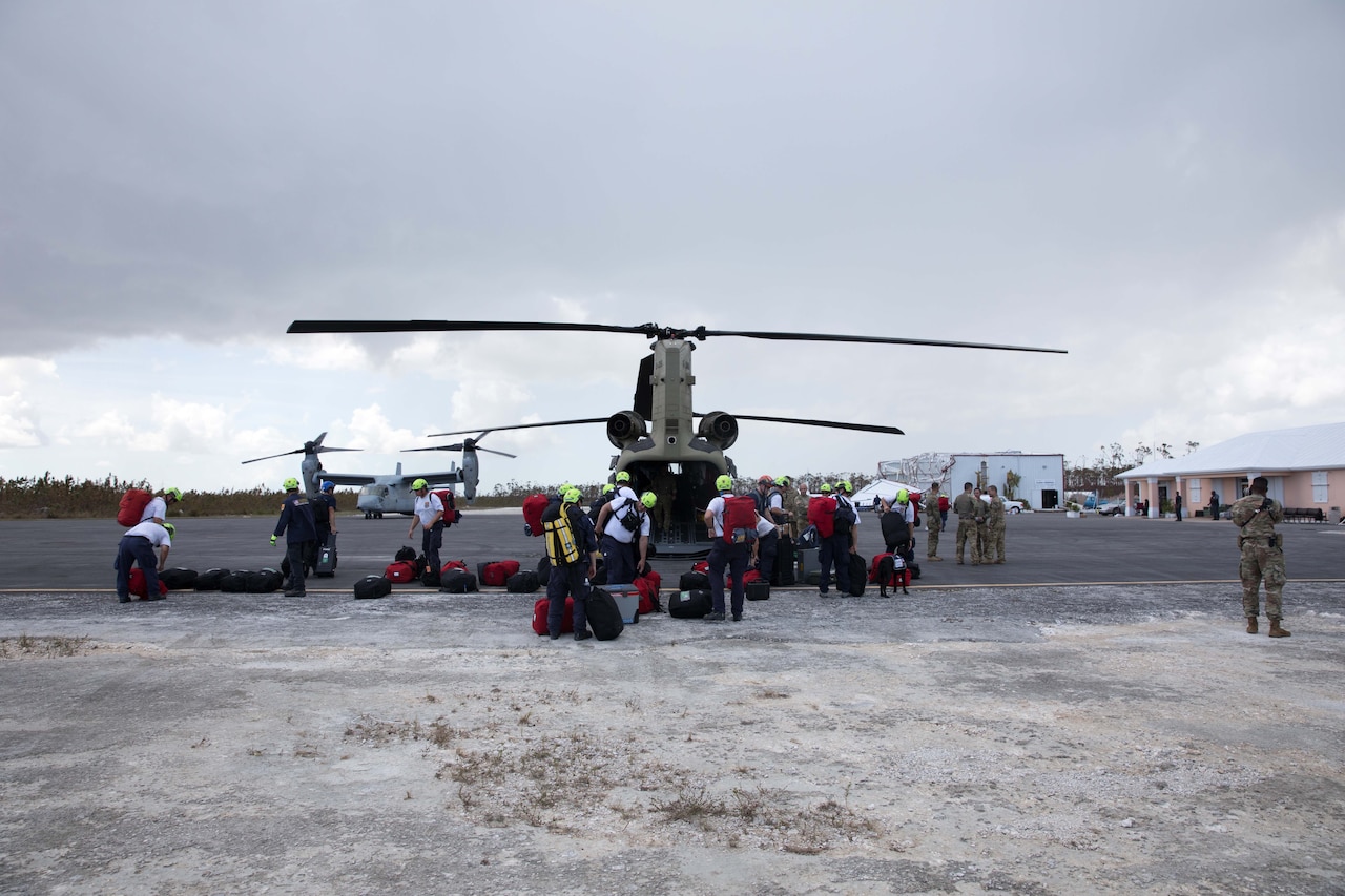 Military and civilian personnel unload a helicopter.