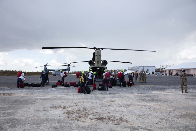 Military and civilian personnel unload a helicopter.