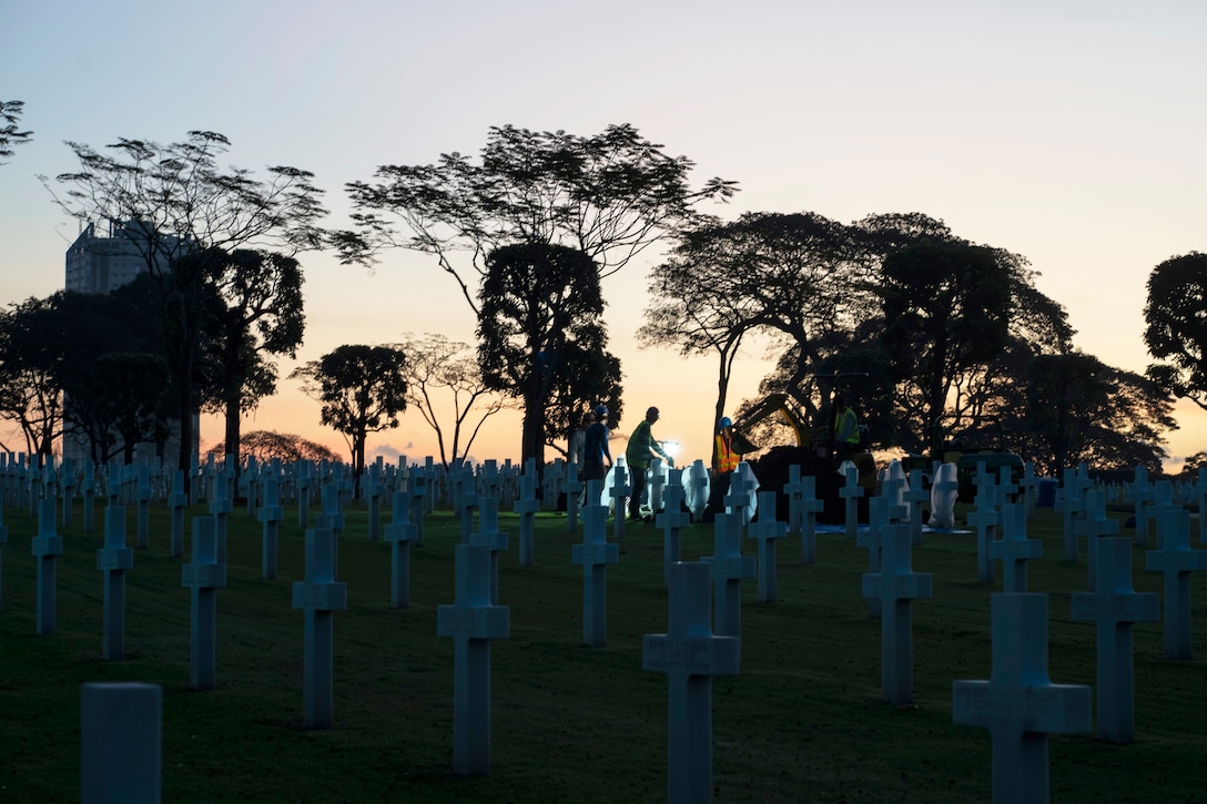 People and construction equipment are silhouetted at twilight in a graveyard.