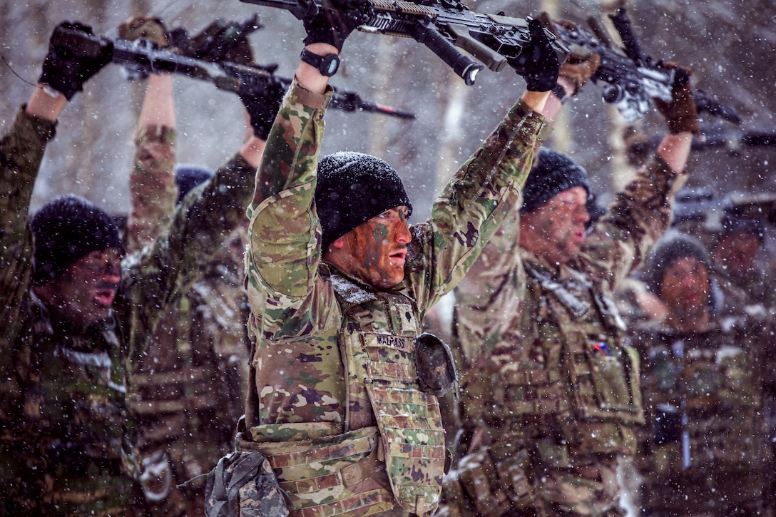 Soldiers hold weapons over their heads while participating in a cold weather battle drill.