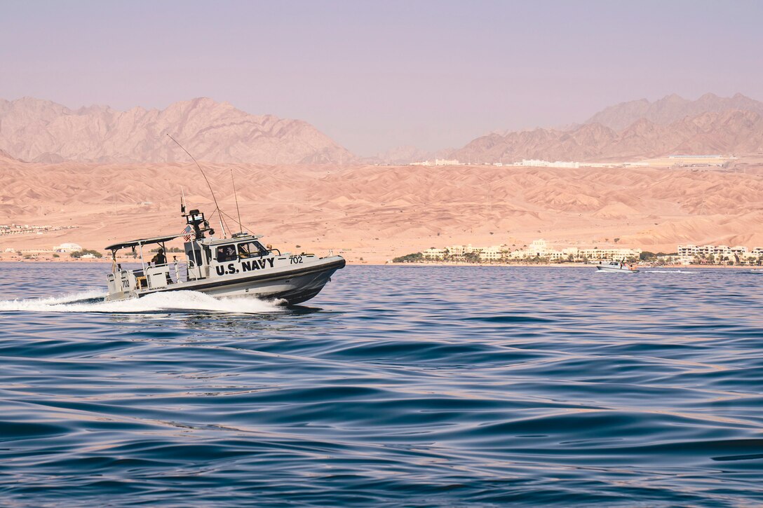 A boat sails in a body of water with mountains in the background.