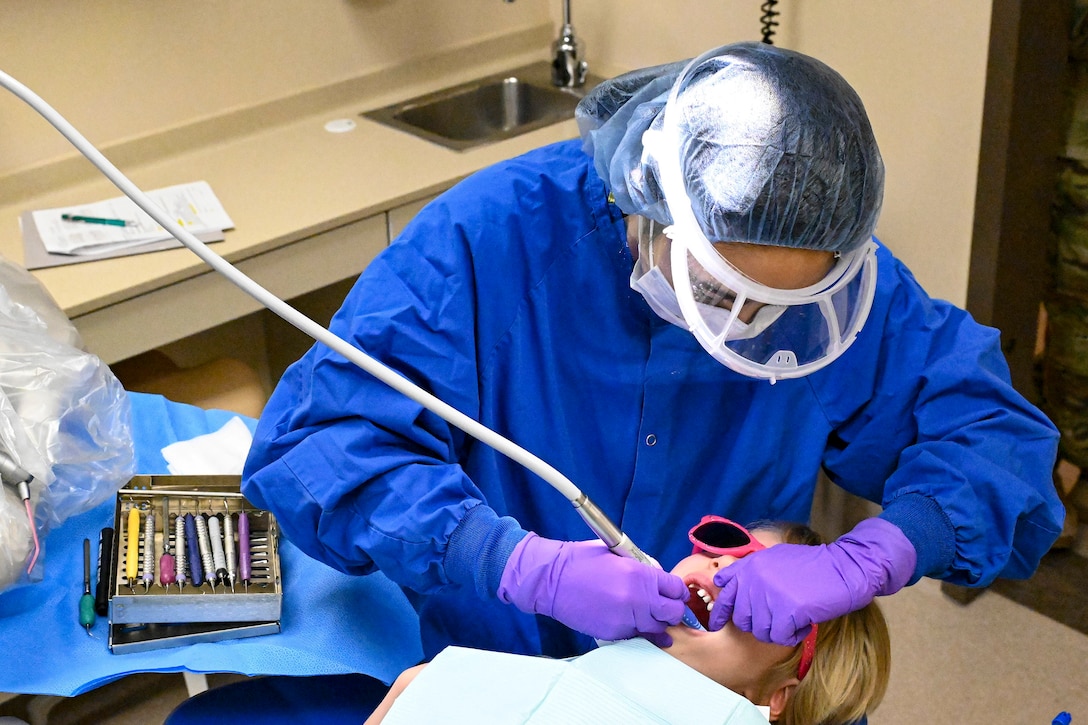 An airman cleans a child’s teeth in a dentist’s office.