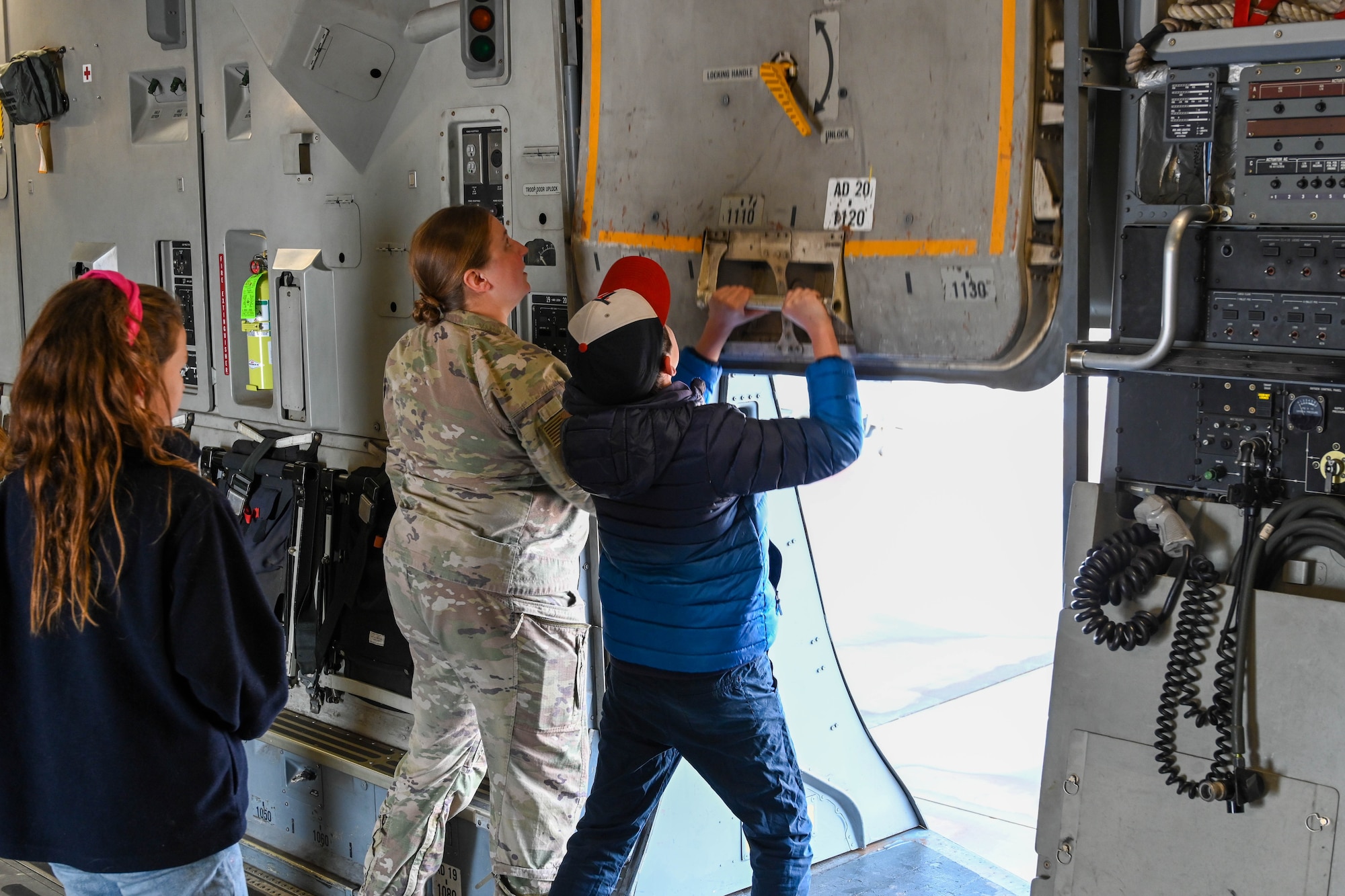U.S. Air Force Staff Sgt. Jacquilyn Mermolia, 58th Airlift Squadron loadmaster instructor, helps Willam Guardiola open a troop door on a C-17 Globemaster III at Altus Air Force Base, Oklahoma, March 14, 2023. Mermolia demonstrated the functions of different parts of the aircraft to showcase C-17 operating procedures. (U.S. Air Force photo by Senior Airman Trenton Jancze)
