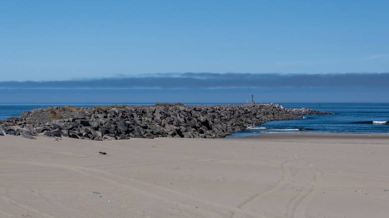 A rock structure extends out from a beach into the ocean on a clear, sunny day.