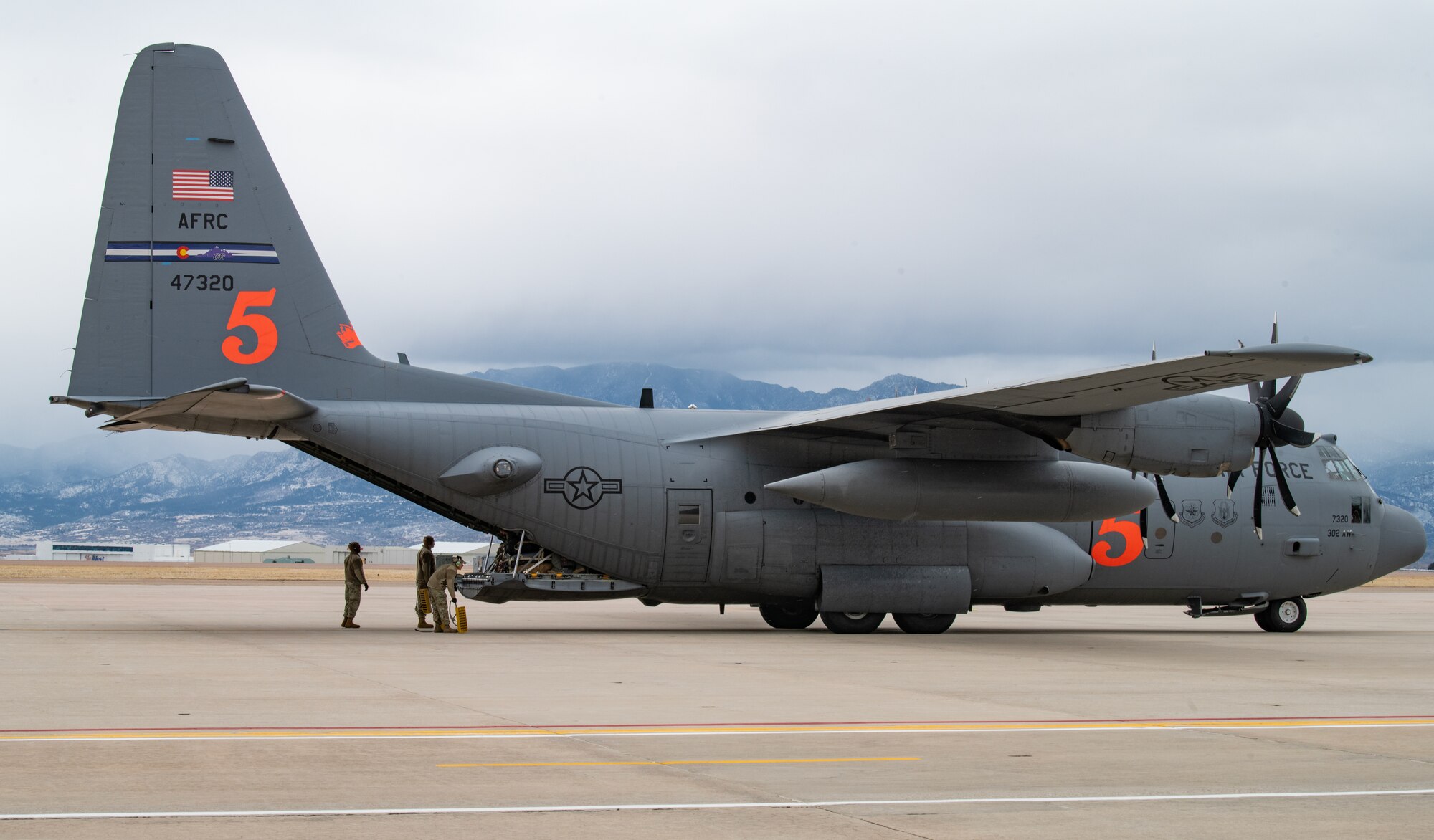 People in military uniforms stand behind military plane as ramp opens