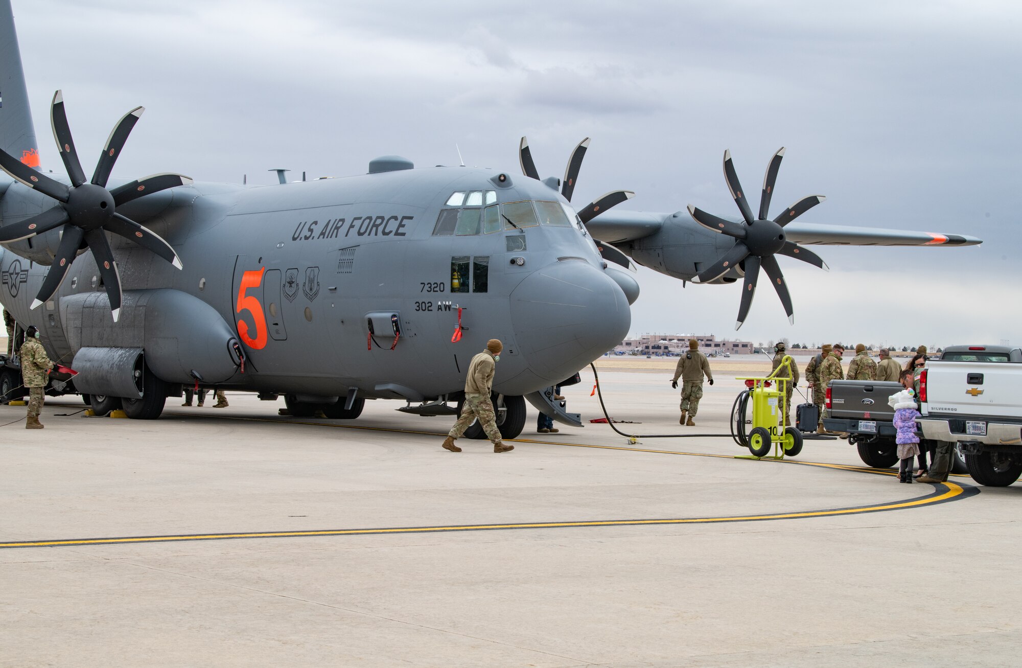 Military cargo plane with eight bladed props sits on flightline with people in military uniform walking around it