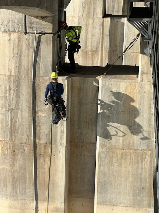 JOHN MARTIN DAM, Colo. – A contractor ropes team scales the nose pier on upstream side of dam, Nov. 8, 2022. Three-person ropes teams installed instrumentation cables and conduit up the face of the dam from borings in the lake, assisted by a dive team. The scaler’s shadow is enhanced by late afternoon sun. Photo by Chris Carroll.