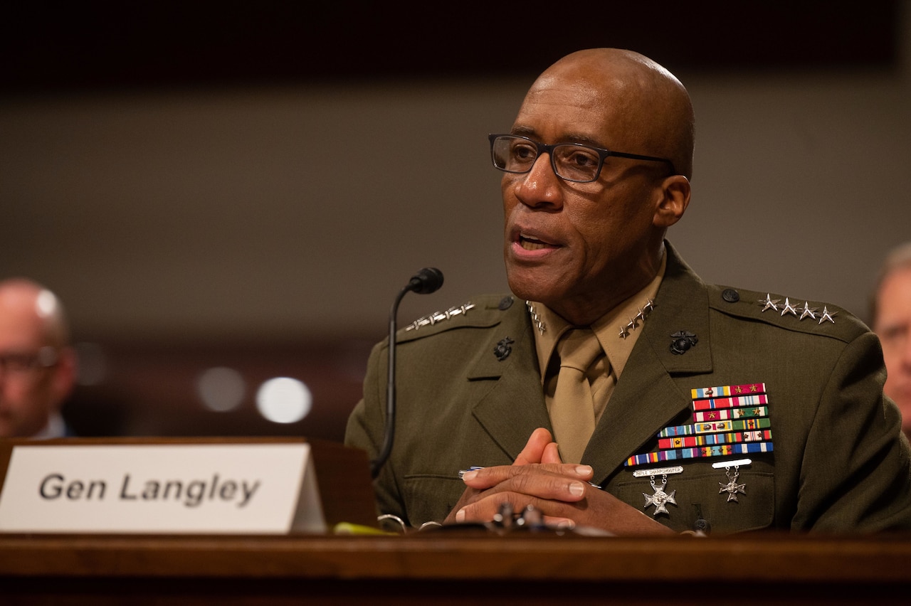 A seated Marine Corps general speaks into a desk mic.