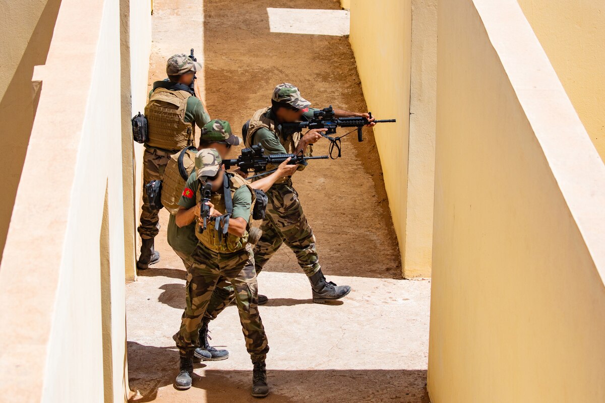 Three men in military uniform point weapons in opposite directions.