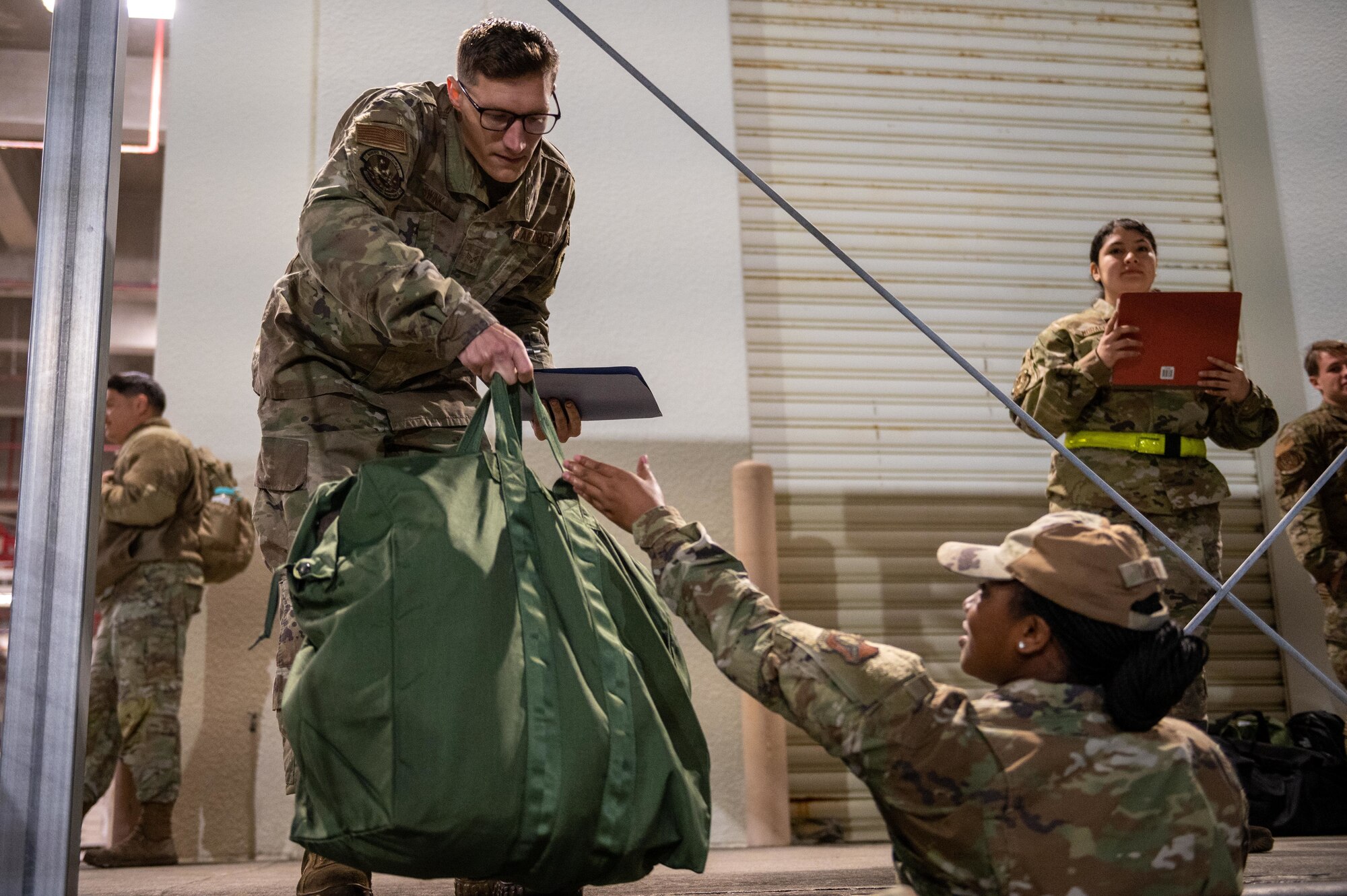 Airman hands green bag to another Airman