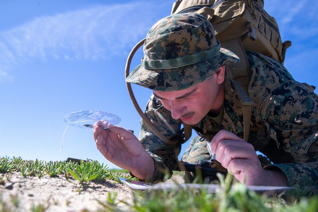 A Marine crouches on the ground and focuses on a map.