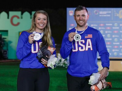 Woman and Man in U.S.A. uniform celebrating with medals in front of ISSF backdrop.