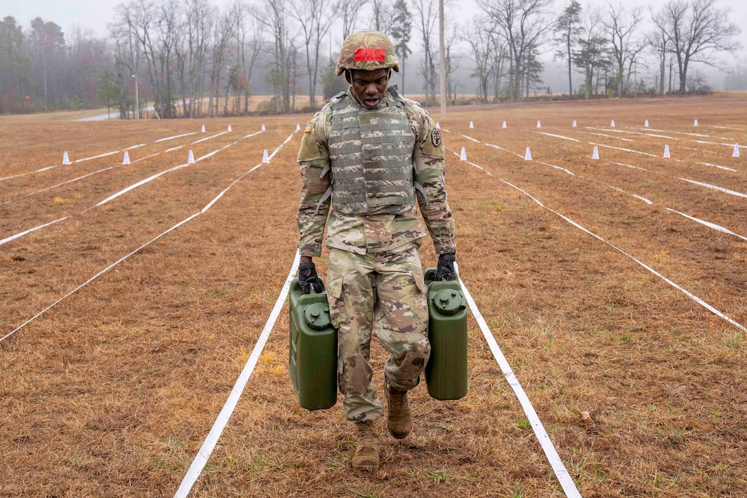 A soldier carries two water containers across a field.