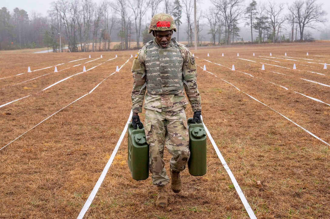 A soldier carries two water containers across a field.