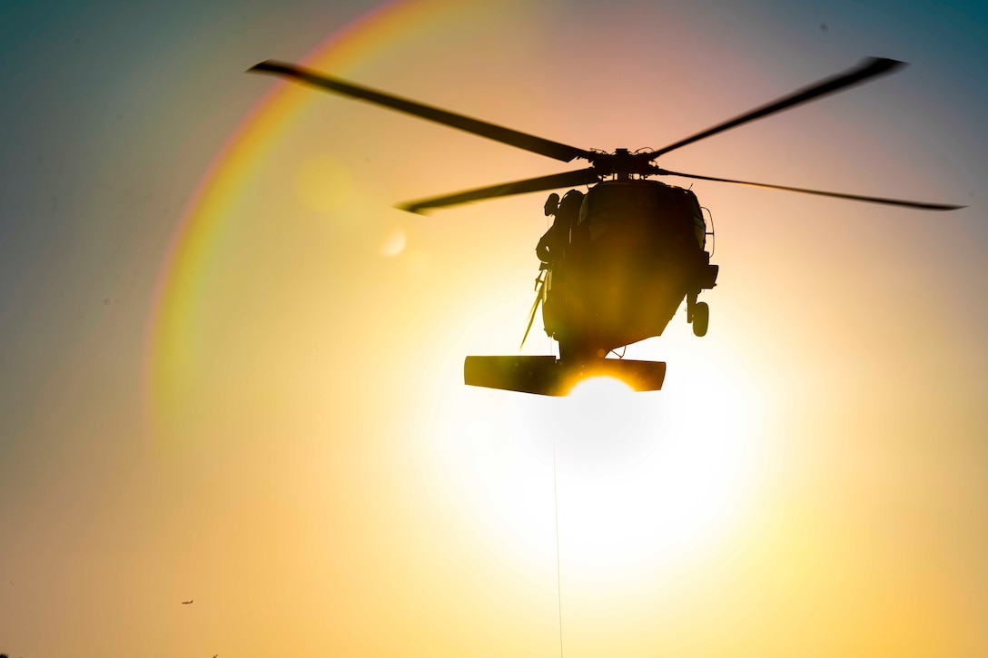 An airborne helicopter shown in silhouette as the sun shines from behind.