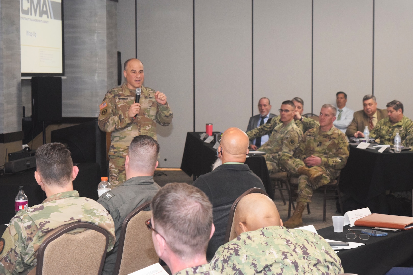 Army general speaks to a room of people, including many in military uniform.
