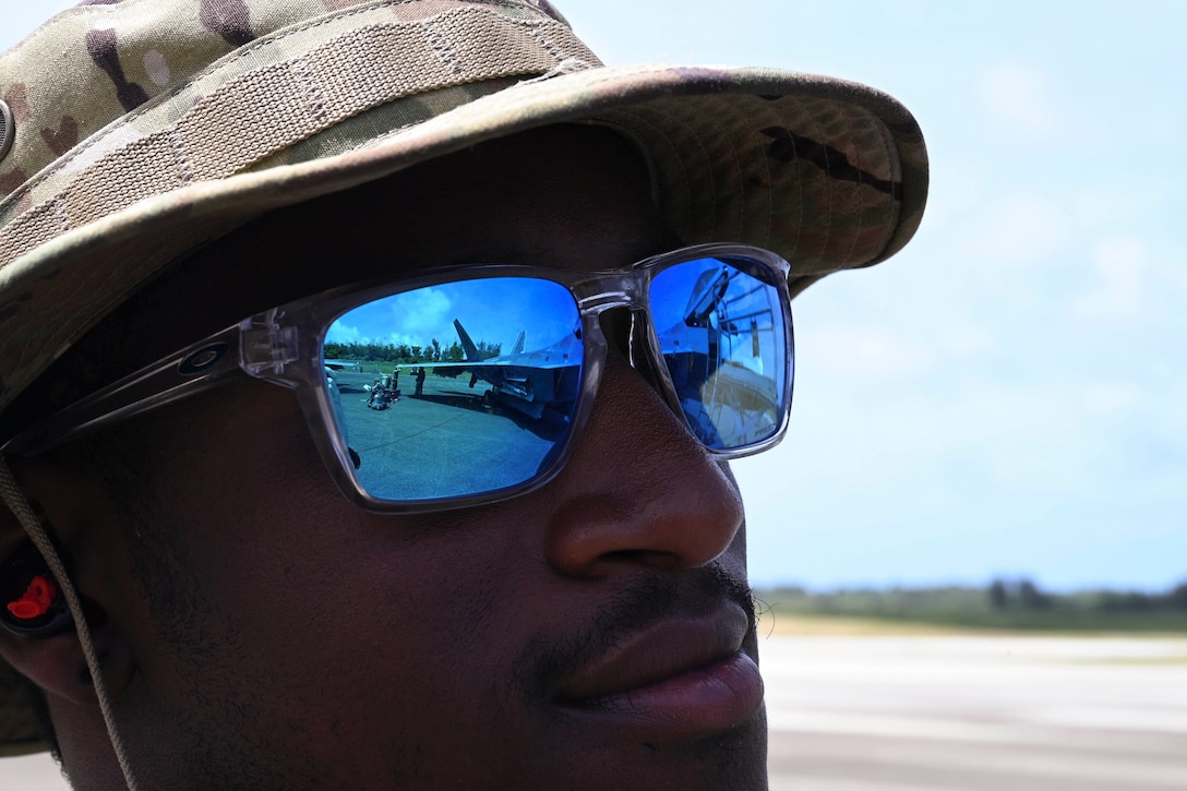 A close shot of an airman wearing sunglasses shows the reflection of an aircraft.
