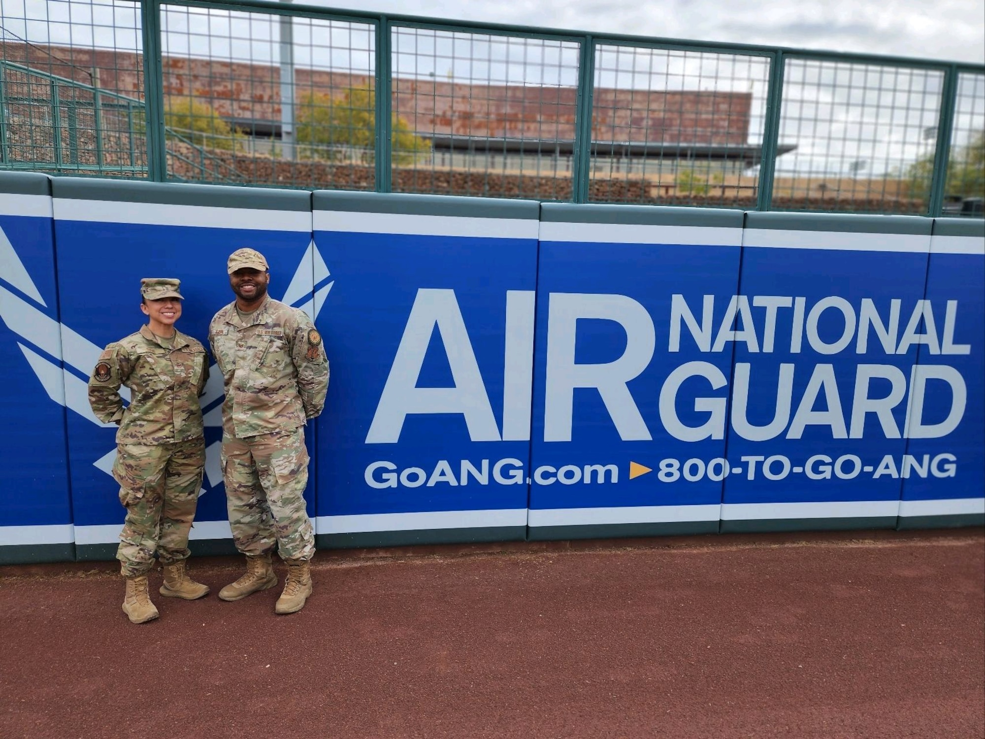 Tech. Sgts. Anna Solis and Glen Eason, production recruiters with the Arizona Air National Guard, pose for a photo in front of the Air National Guard outfield banner at Camelback Ranch–Glendale baseball complex in Phoenix, March 1, 2023.