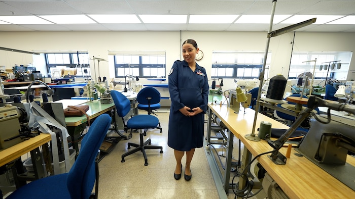 Pregnant Female Airmen poses in service dress the middle of photo with sewing supplies around her.