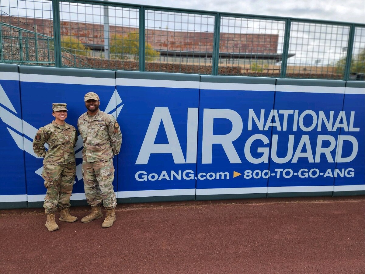 Tech. Sgts. Anna Solis and Glen Eason, production recruiters with the Arizona Air National Guard, pose for a photo in front of the Air National Guard outfield banner at Camelback Ranch–Glendale baseball complex in Phoenix, March 1, 2023.