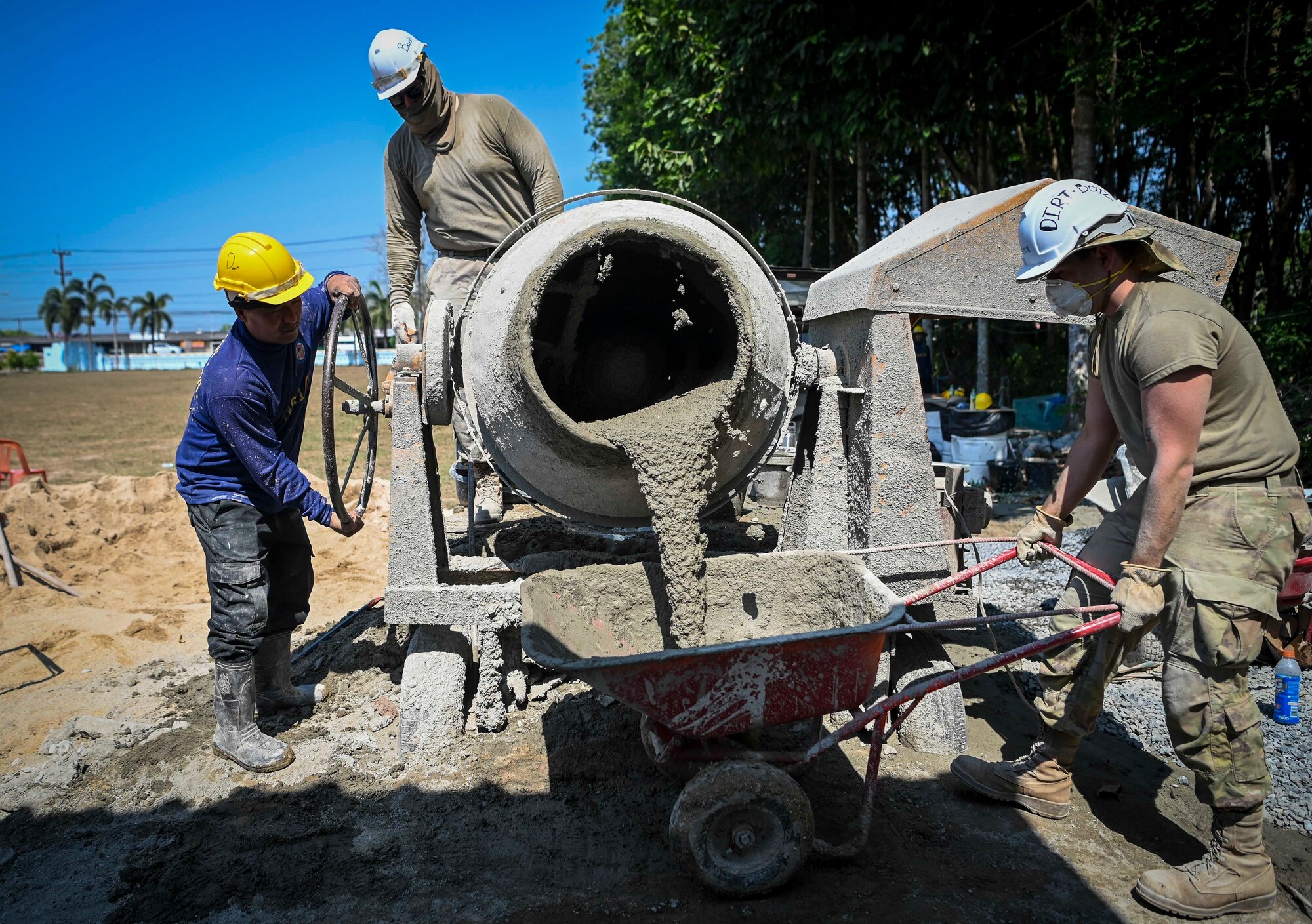 Three engineers pour concrete out of a mixer into a wheelbarrow.