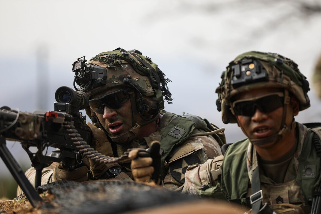 A soldier looks through the scope of a weapon with a second soldier beside him.