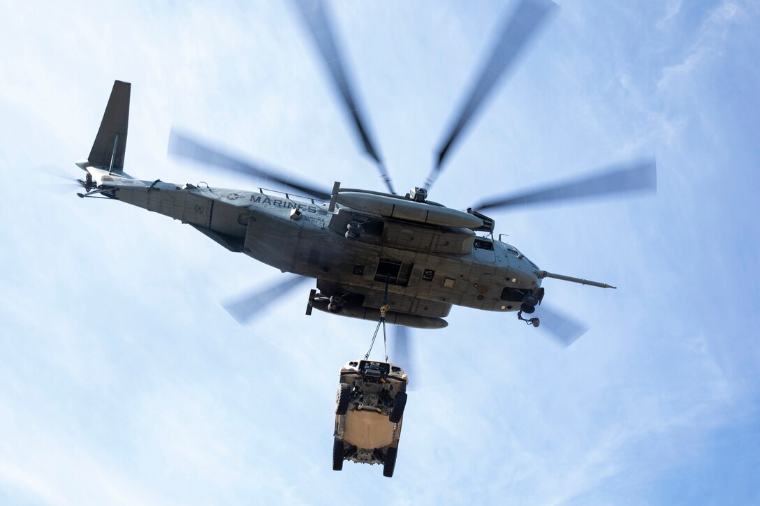 A military helicopter tows a vehicle.