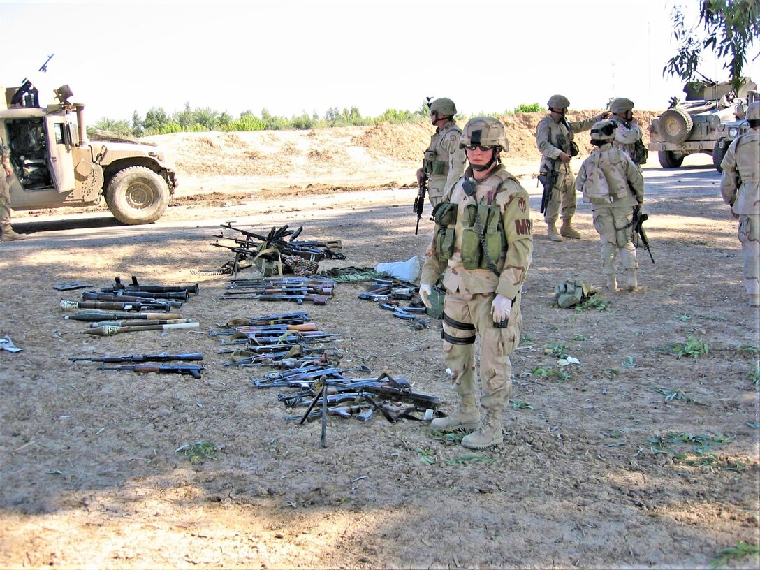 Sgt. Leigh Ann Hester, team leader, 4th Platoon, 617th Military Police Company, 503rd MP Battalion, 18th MP Brigade, stands in front of a captured weapons cache after her squad repelled an insurgent attack on a Coalition supply convoy March 20, 2005, about 18 miles southeast of Baghdad. Twenty-seven insurgents were killed, one was captured and six were injured. Hester is from Bowling Green, Ky. (U.S. Army photo by Sgt. 1st Class Marshall P. Ware)