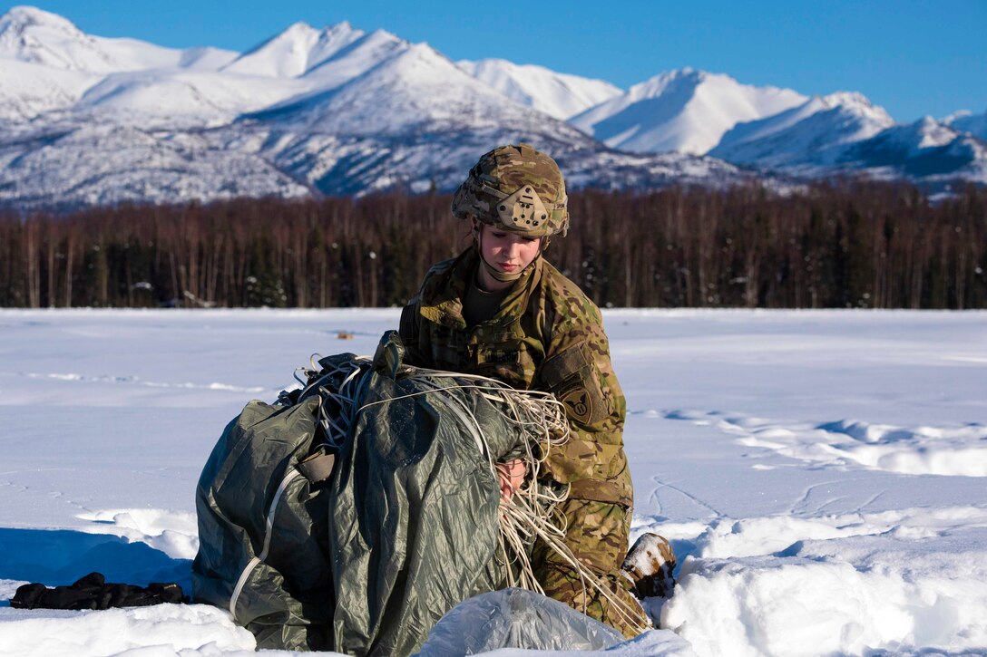 A soldier picks up a parachute on snow-covered ground.