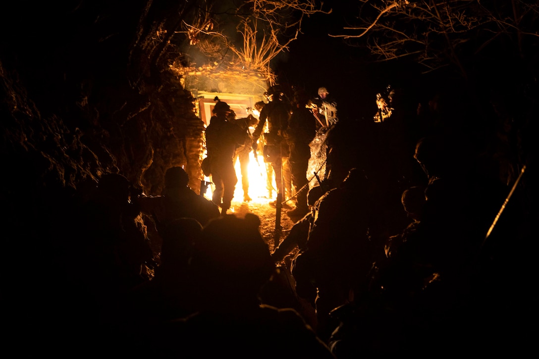 Soldiers gather inside a dark underground tunnel with light shining at the end.