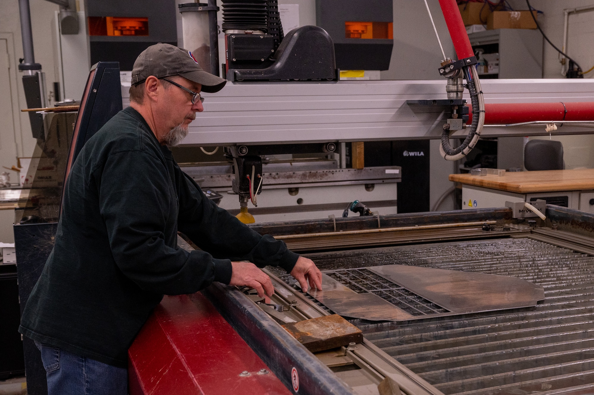 Don Elder, Detachment 9 aerospace mechanical technician, places a metal sheet on a water jet cutting machine, Mar. 13, 2023, at Luke Air Force Base, Arizona.