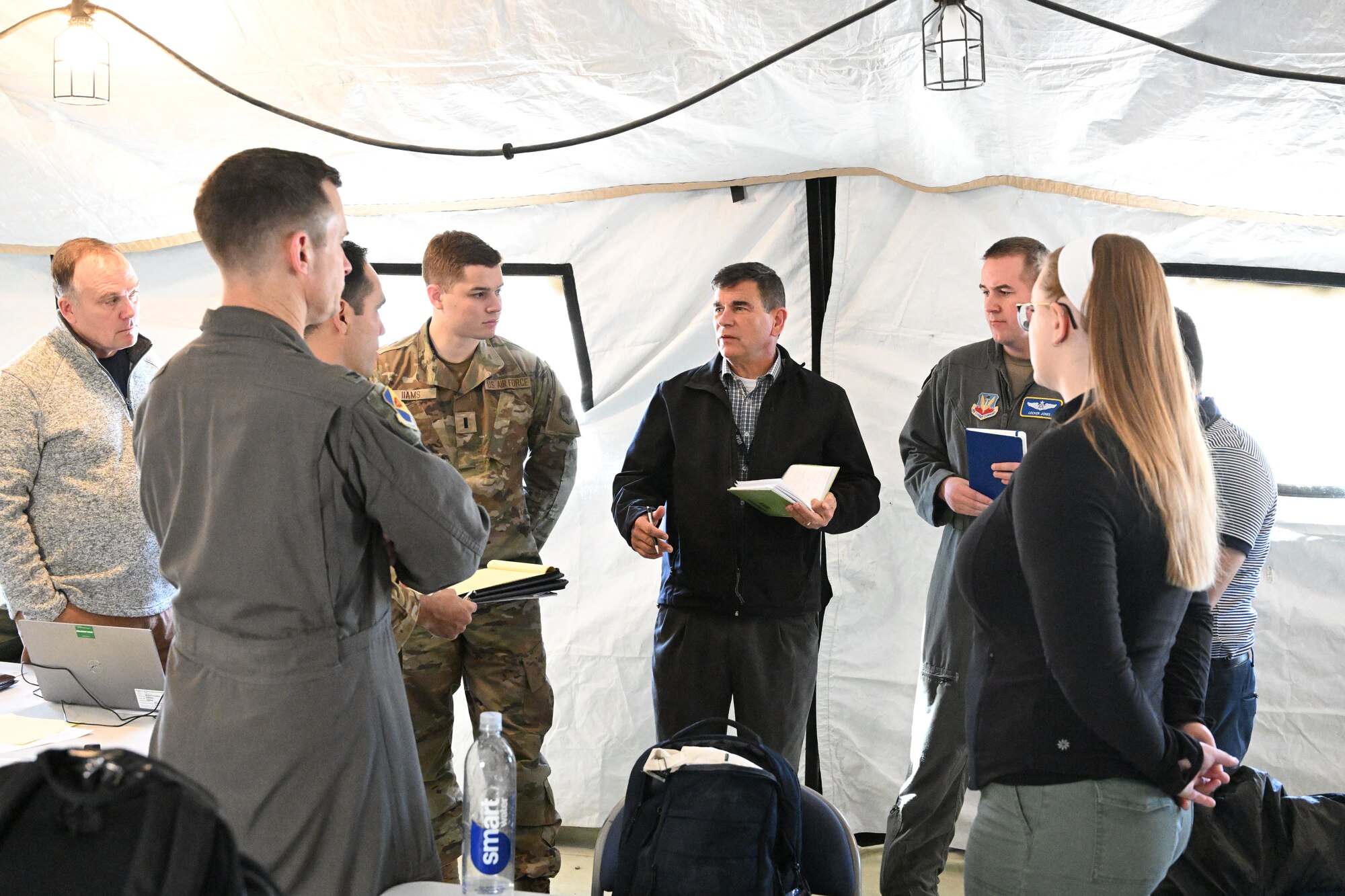 photo of four uniformed U.S. Air Force military members and five civilians standing in a circle in a tent talking