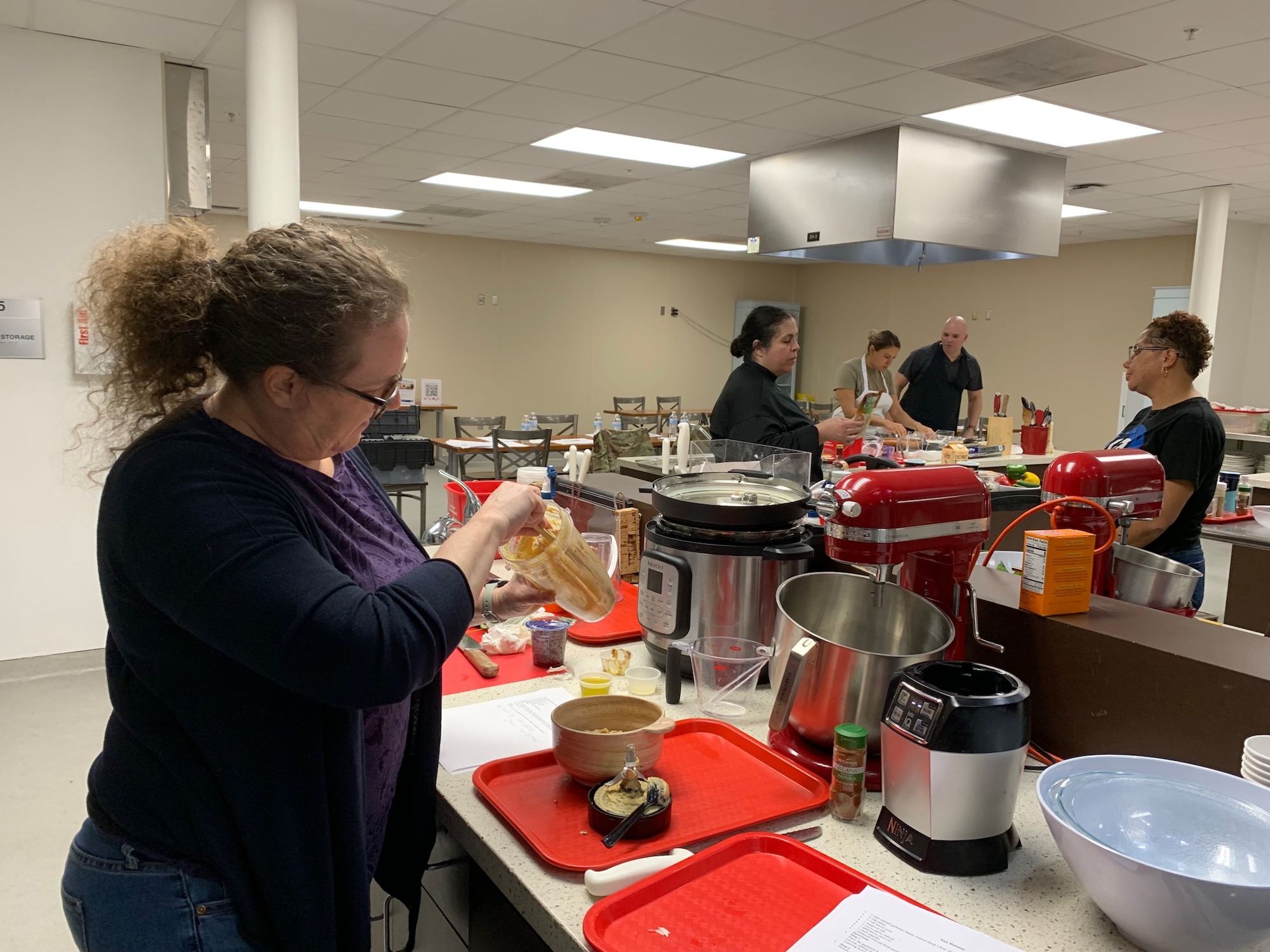 K.C. Erredge, Key Spouse Mentor of the 960th Cyberspace Wing, prepares "Easy Hummus" while other members receive instruction on their dish. (Courtesy photo)