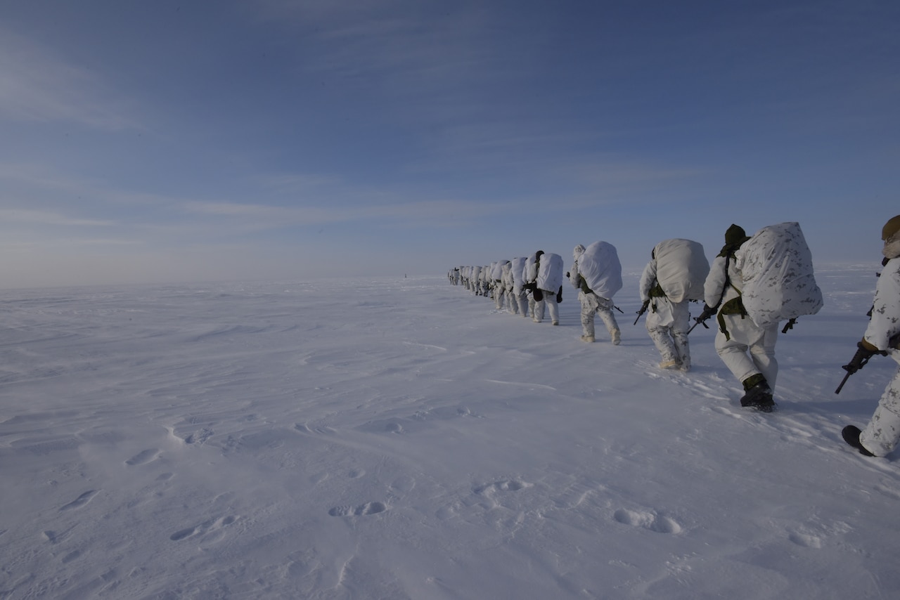 Soldiers walk in a line through snow.